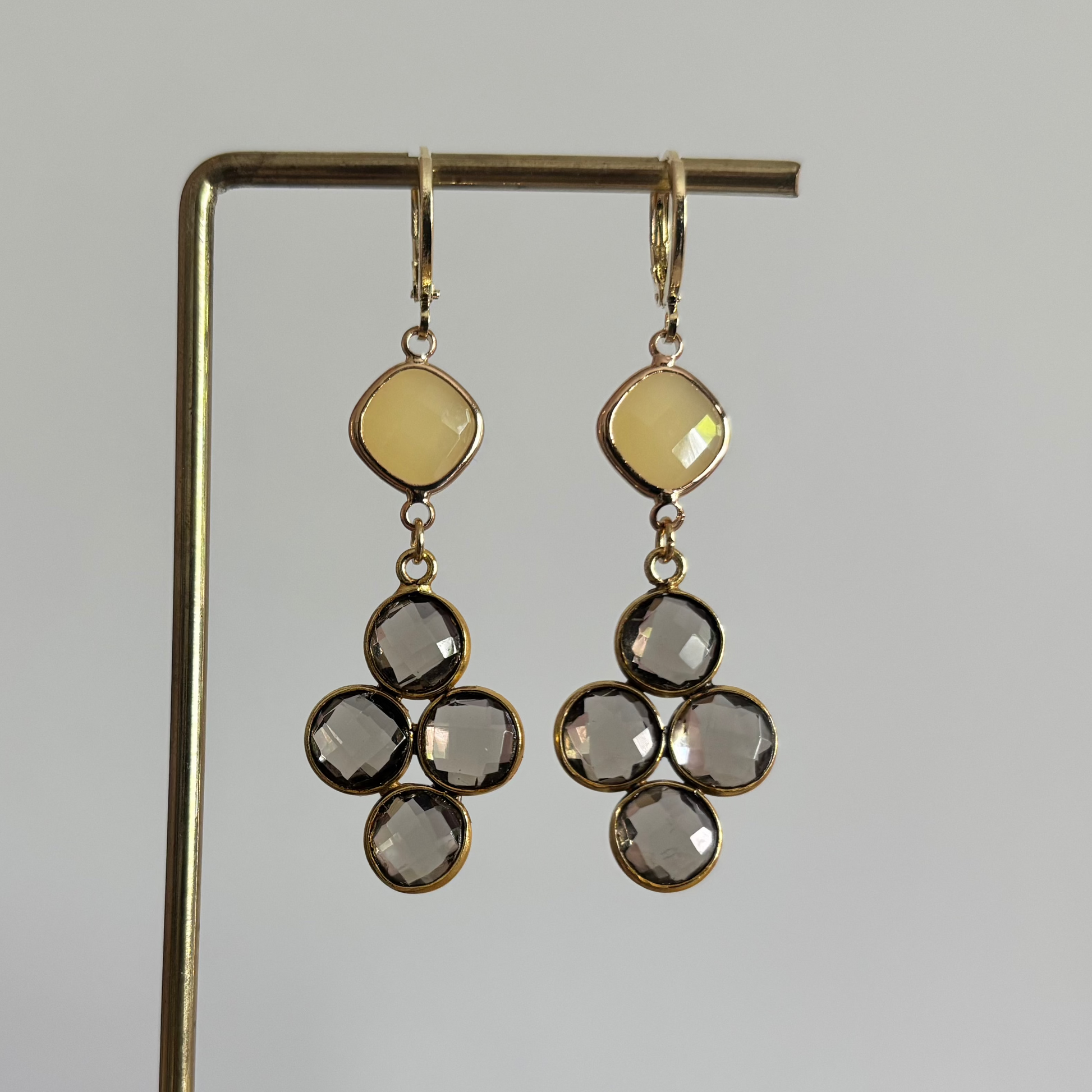 Gouden oorbellen Holly met een ruitvormige gele steen en een hanger van vier taupekleurige facetgeslepen steentjes op een standaard