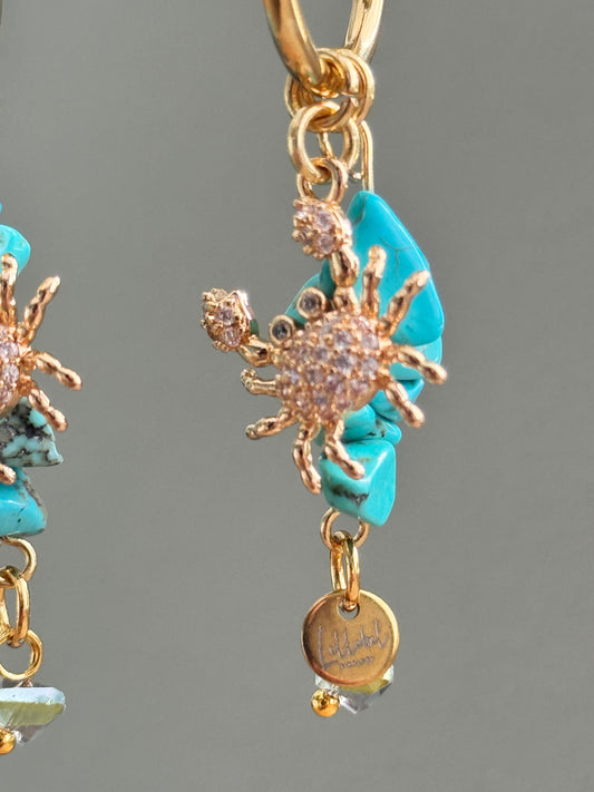 detailfoto van 18K vergulde krab ingelegd met zirkonia hangend aan een oorbel met rvs hoops en turquoise natuurstenen
