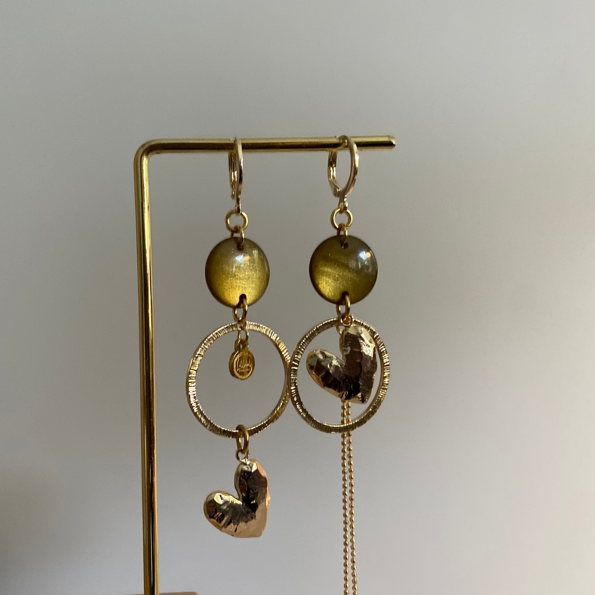 Asymmetrische 14k vergulde oorbellen met mosgroene cabochon, gehamerde ringen, hartbedel en klein kwastje, ca. 6 cm lang.