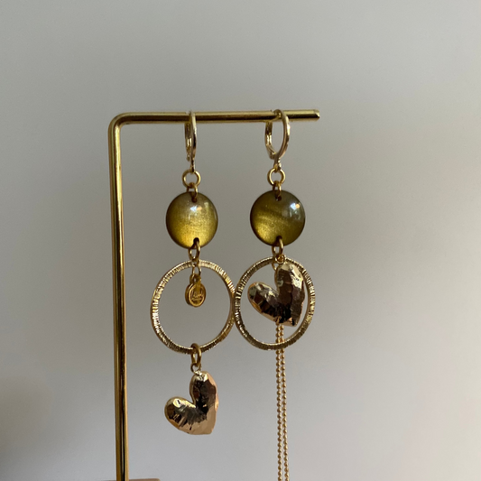 Asymmetrische 14k vergulde oorbellen met mosgroene cabochon, gehamerde ringen, hartbedel en klein kwastje, ca. 6 cm lang.
