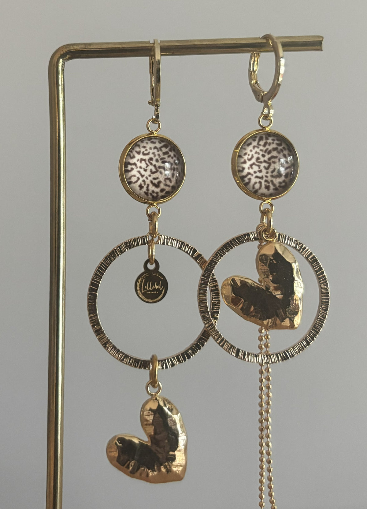 Asymmetrische 14k vergulde oorbellen Ivy met panterprint cabochon, gehamerde ringen, hartvormige bedel en kwastje, circa 6 cm lang