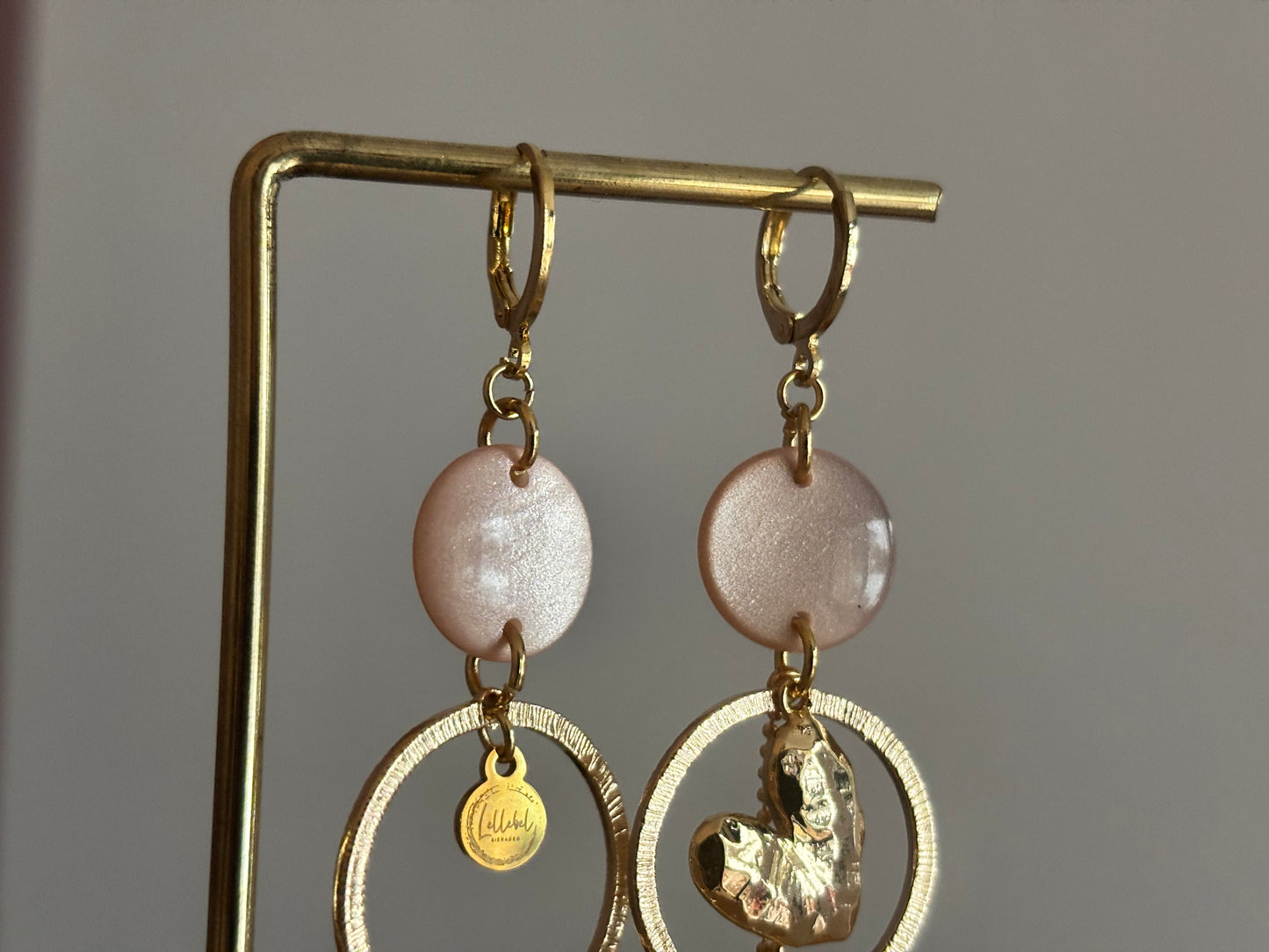 Asymmetrische 14k vergulde oorbellen Ivy met parelmoer zachtroze cabochon, gehamerde ringen, hartvormige bedel en kwastje, circa 6 cm lang