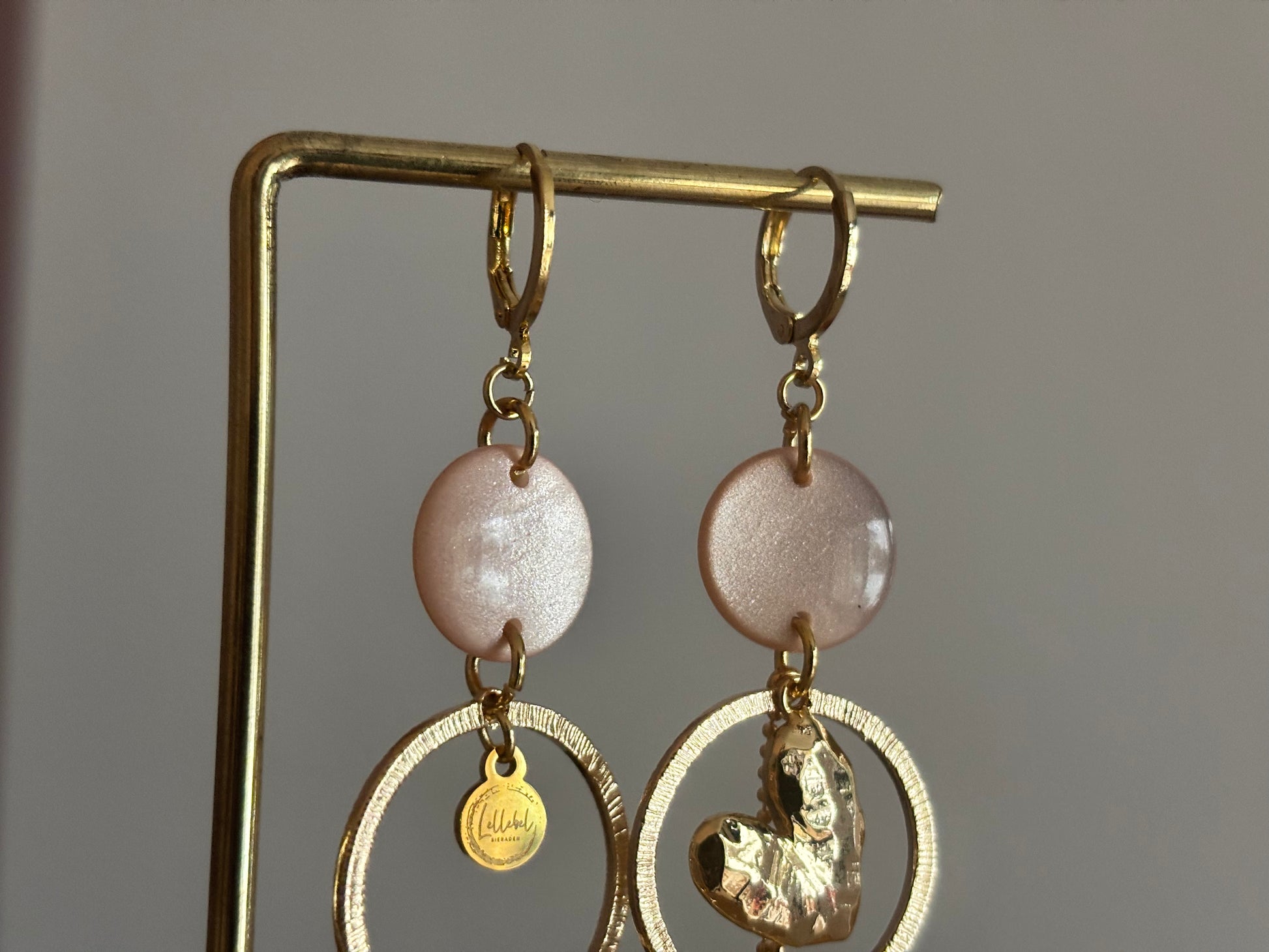 Asymmetrische 14k vergulde oorbellen Ivy met parelmoer zachtroze cabochon, gehamerde ringen, hartvormige bedel en kwastje, circa 6 cm lang