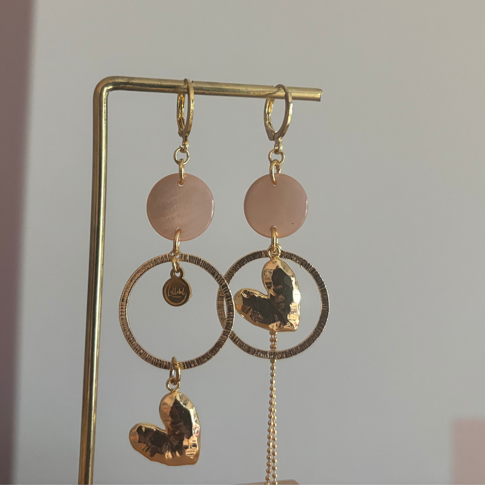 Asymmetrische 14k vergulde oorbellen Ivy met zachtroze cabochon, gehamerde ringen, hartvormige bedel en kwastje, circa 7 cm lang