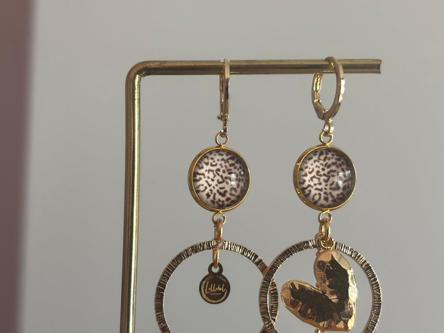 Asymmetrische 14k vergulde oorbellen Ivy met panterprint cabochon, gehamerde ringen, hartvormige bedel en kwastje, circa 6 cm lang