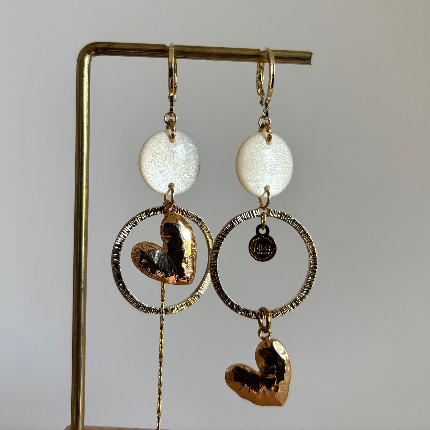 Asymmetrische 14k vergulde oorbellen Ivy met witte parelmoer cabochon, gehamerde ringen, hartvormige bedel en kwastje, circa 7 cm lang