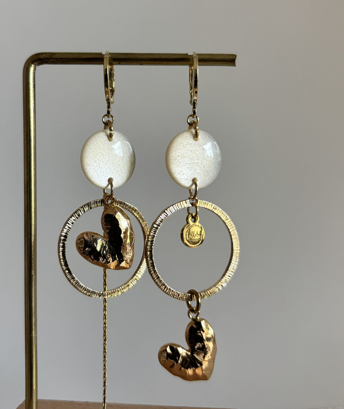 Asymmetrische 14k vergulde oorbellen Ivy met witte parelmoer cabochon, gehamerde ringen, hartvormige bedel en kwastje, circa 7 cm lang