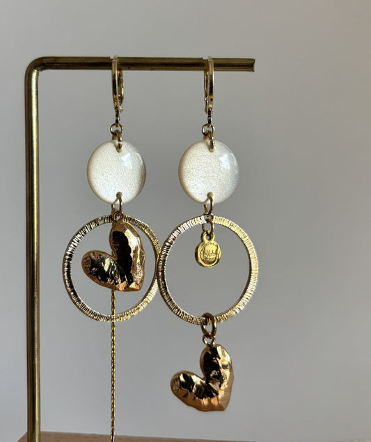 Asymmetrische 14k vergulde oorbellen Ivy met witte parelmoer cabochon, gehamerde ringen, hartvormige bedel en kwastje, circa 7 cm lang