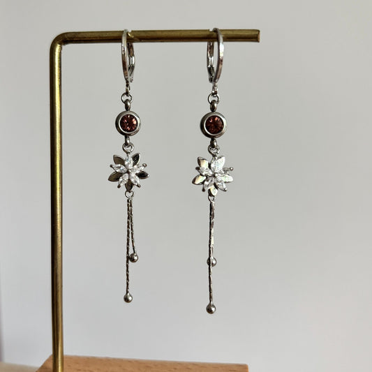 Zilverkleurige hangoorbellen Jasmijn met ingezet oudroze kristal, glinsterend zirkonia bloemetje en twee neerhangende kettinkjes met bolletjes.