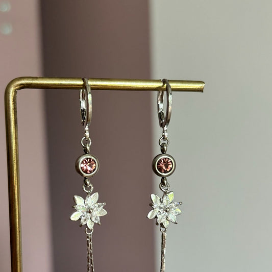Zilverkleurige hangoorbellen Jasmijn met ingezet oudroze kristal, glinsterend zirkonia bloemetje en twee neerhangende kettinkjes met bolletjes.