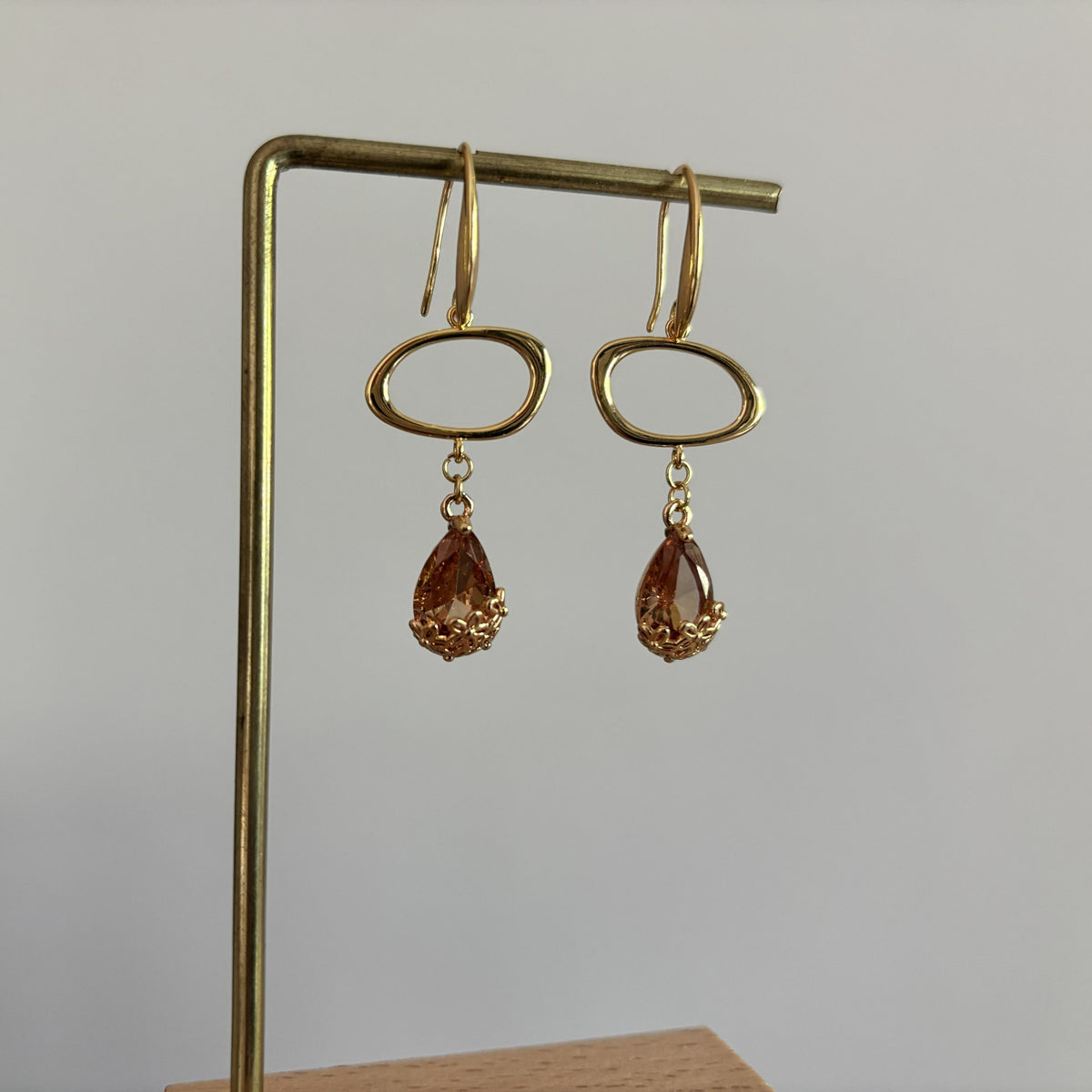 14k vergulde oorbellen Jinke met een liggende open ovale ring en een gefacetteerde amberkleurige kristal druppel.