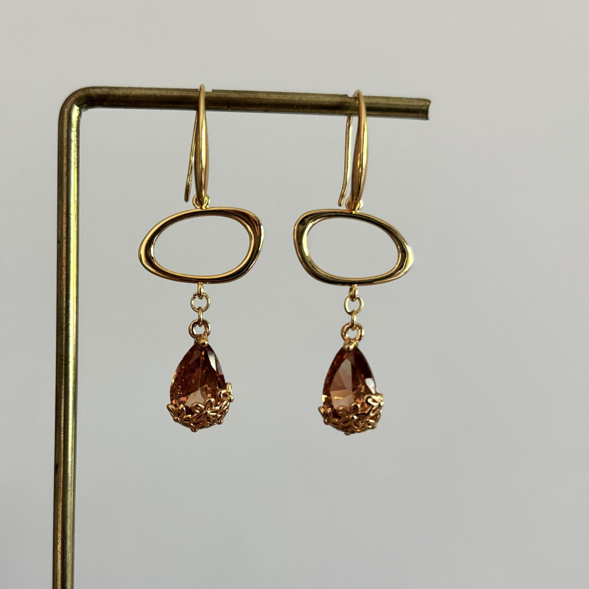 14k vergulde oorbellen Jinke met een liggende open ovale ring en een gefacetteerde amberkleurige kristal druppel.