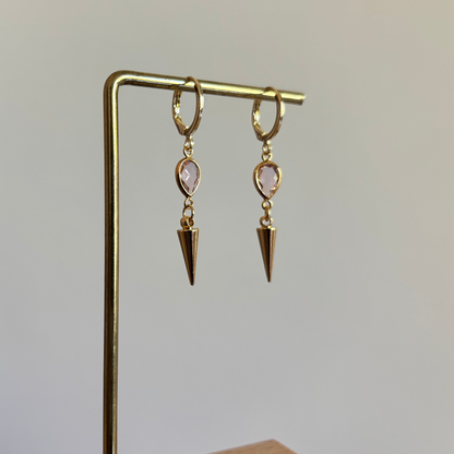 Goudkleurige oorbellen met een kleine roze druppelvormige steen en een hangende goudkleurige spike bedel."
