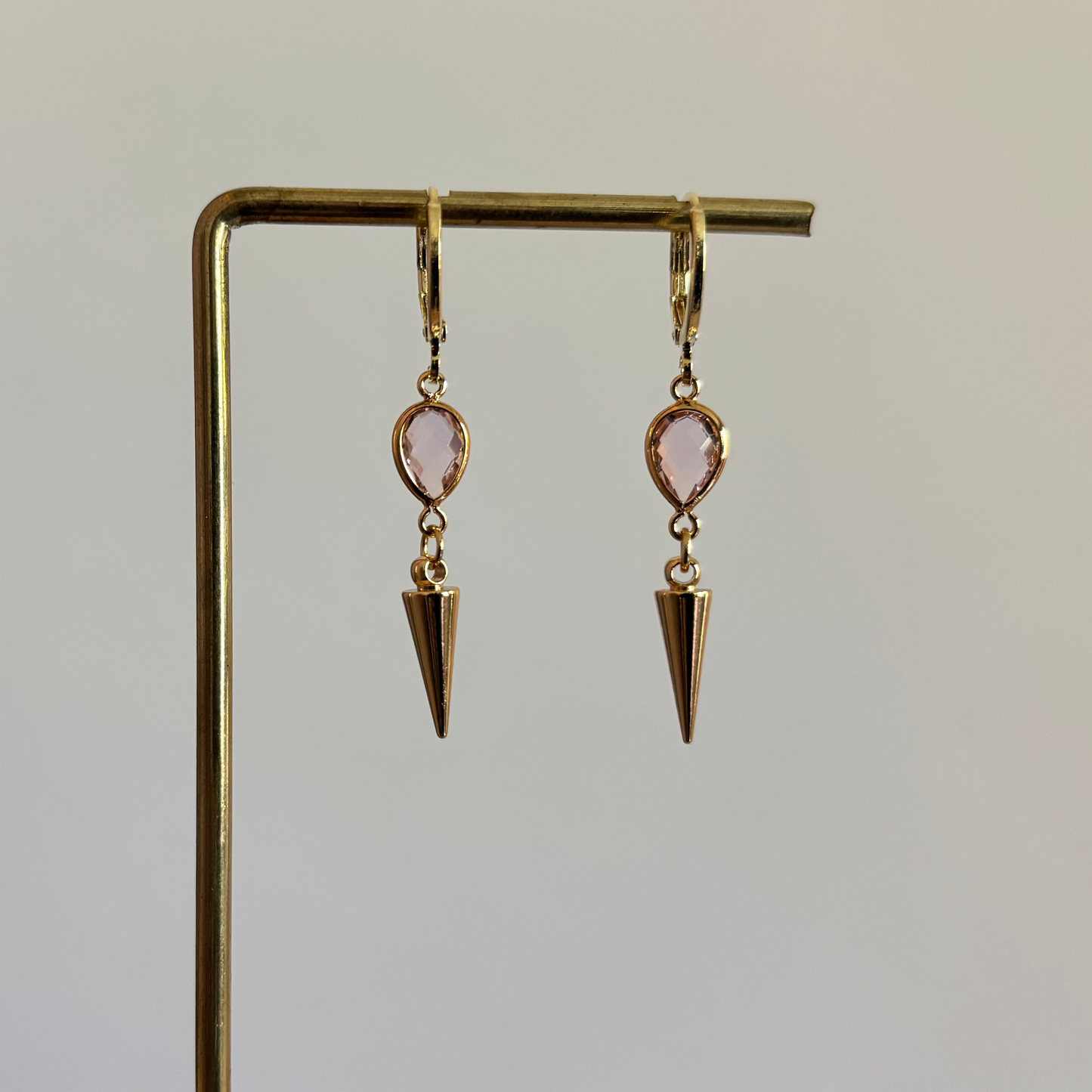 Goudkleurige oorbellen met een kleine roze druppelvormige steen en een hangende goudkleurige spike bedel."