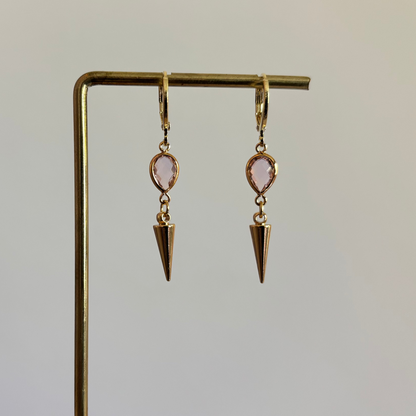Goudkleurige oorbellen met een kleine roze druppelvormige steen en een hangende goudkleurige spike bedel."