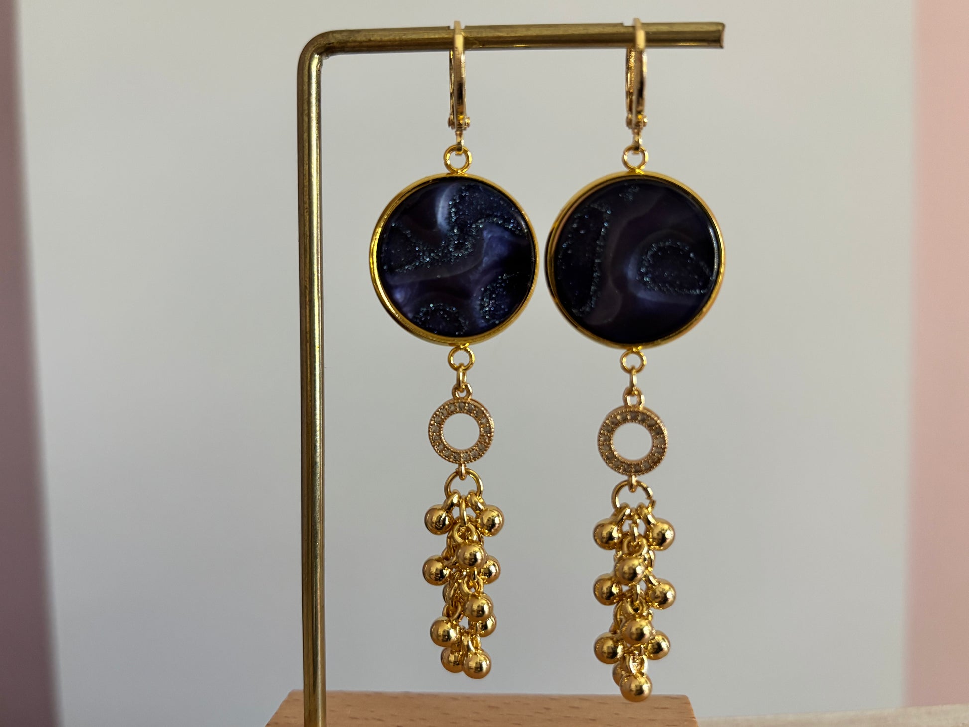 Goudkleurige oorbellen Joke met een donkerblauwe glinsterende polaris steen, strass-ringetje en goudkleurig bollentrosje