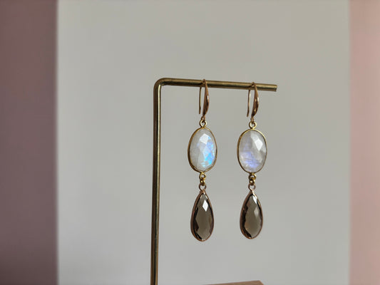 Lange 14k vergulde oorbellen 'Kyra' met een ovale melkwitte maansteen en een facetgeslepen taupe druppelhanger in een gouden omlijsting.