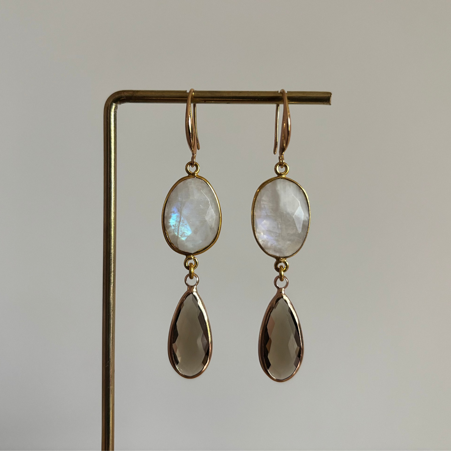 Lange 14k vergulde oorbellen 'Kyra' met een ovale melkwitte maansteen en een facetgeslepen taupe druppelhanger in een gouden omlijsting.