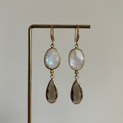 Lange 14k vergulde oorbellen 'Kyra' met een ovale melkwitte maansteen en een facetgeslepen taupe druppelhanger in een gouden omlijsting.