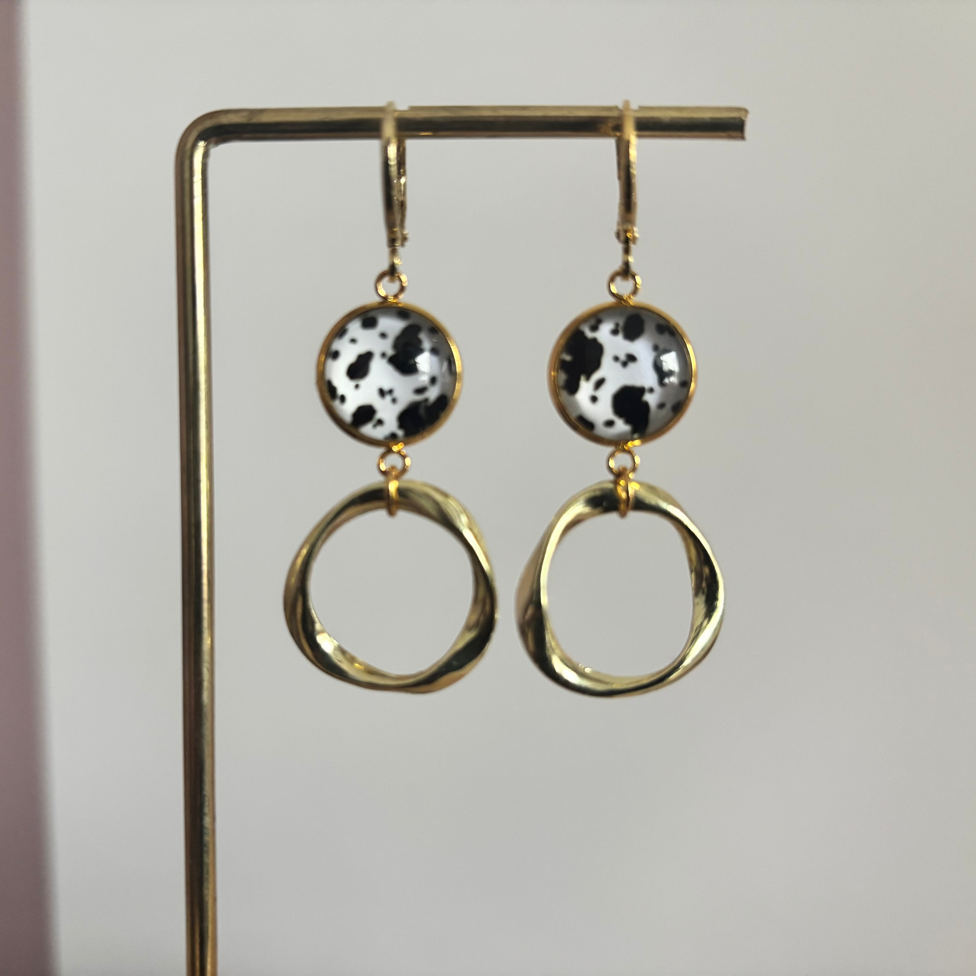 Gouden oorbellen Lian met ronde zwart-wit gevlekte hangers en organisch gevormde gouden ringen op een standaard.