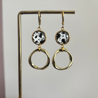 Gouden oorbellen Lian met ronde zwart-wit gevlekte hangers en organisch gevormde gouden ringen op een standaard.