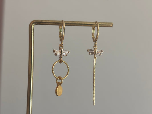 Asymmetrische oorbellen met zirkonia libelles, één met strengetje en één met minimalistische hanger en Lellebel-tag, circa 4 cm lang.