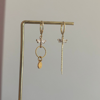 Asymmetrische oorbellen met zirkonia libelles, één met strengetje en één met minimalistische hanger en Lellebel-tag, circa 4 cm lang.