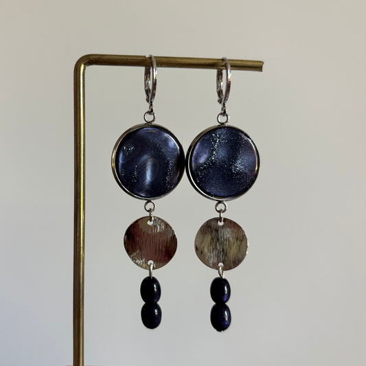 Zilverkleurige gelaagde oorbellen Linde Donkerblauw Zilver met marmerlook cabochon, geborsteld metalen rondje en twee donkerblauwe kralen.