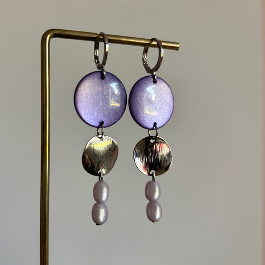 Zilverkleurige gelaagde oorbellen Linde Lila Zilver met parelmoerglans cabochon, geborsteld metalen rondje en twee lila kralen.