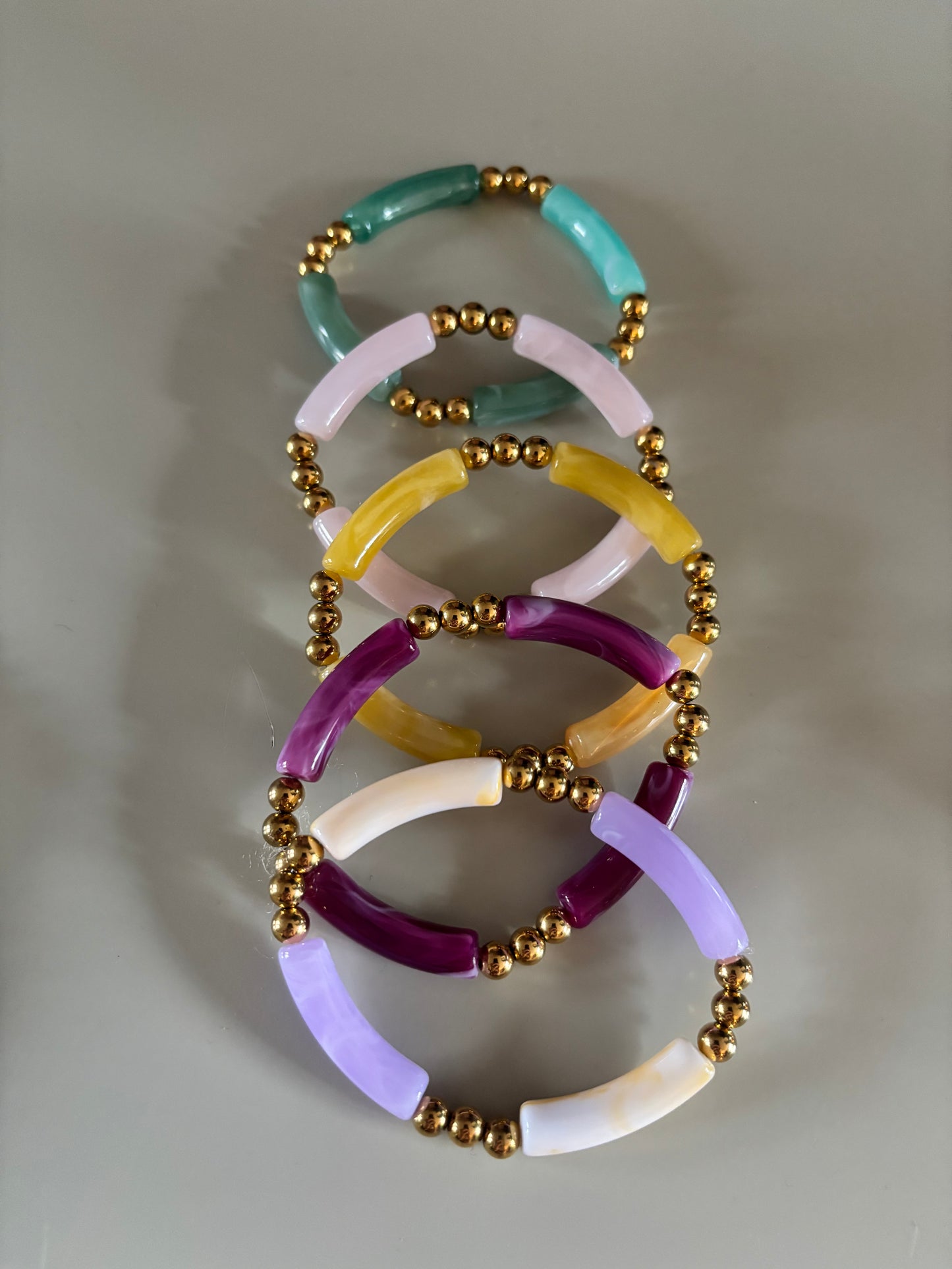 8k goldplated bolletjes en een grote, gebogen kunststof kraal met een subtiel gemarmerd effect in diverse kleuren zoals lila, fuchsia, oranje en mintgroen, paars, okergeel, koraal, zeegroen.