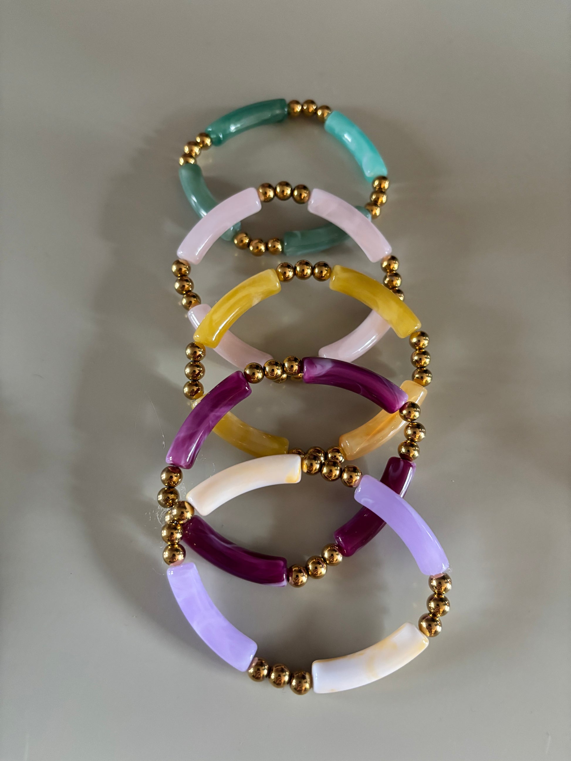 8k goldplated bolletjes en een grote, gebogen kunststof kraal met een subtiel gemarmerd effect in diverse kleuren zoals lila, fuchsia, oranje en mintgroen, paars, okergeel, koraal, zeegroen.