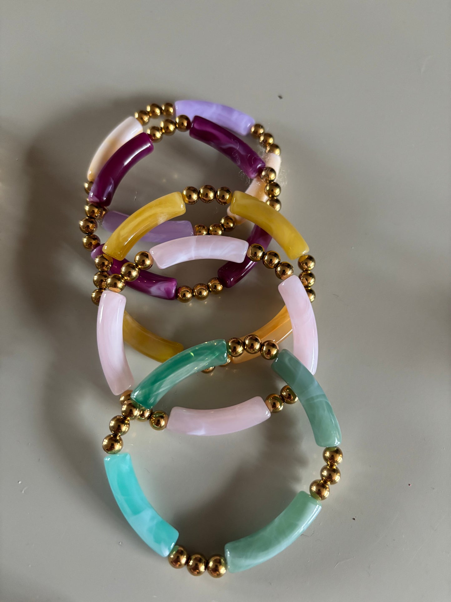 8k goldplated bolletjes en een grote, gebogen kunststof kraal met een subtiel gemarmerd effect in diverse kleuren zoals lila, fuchsia, oranje en mintgroen, paars, okergeel, koraal, zeegroen.