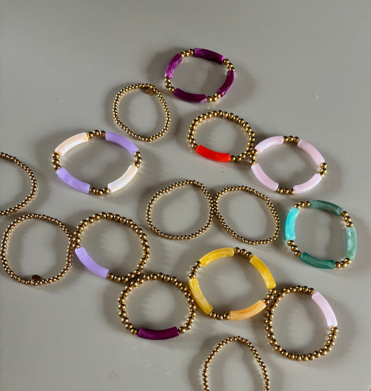 8k goldplated bolletjes en een grote, gebogen kunststof kraal met een subtiel gemarmerd effect in diverse kleuren zoals lila, fuchsia, oranje en mintgroen.