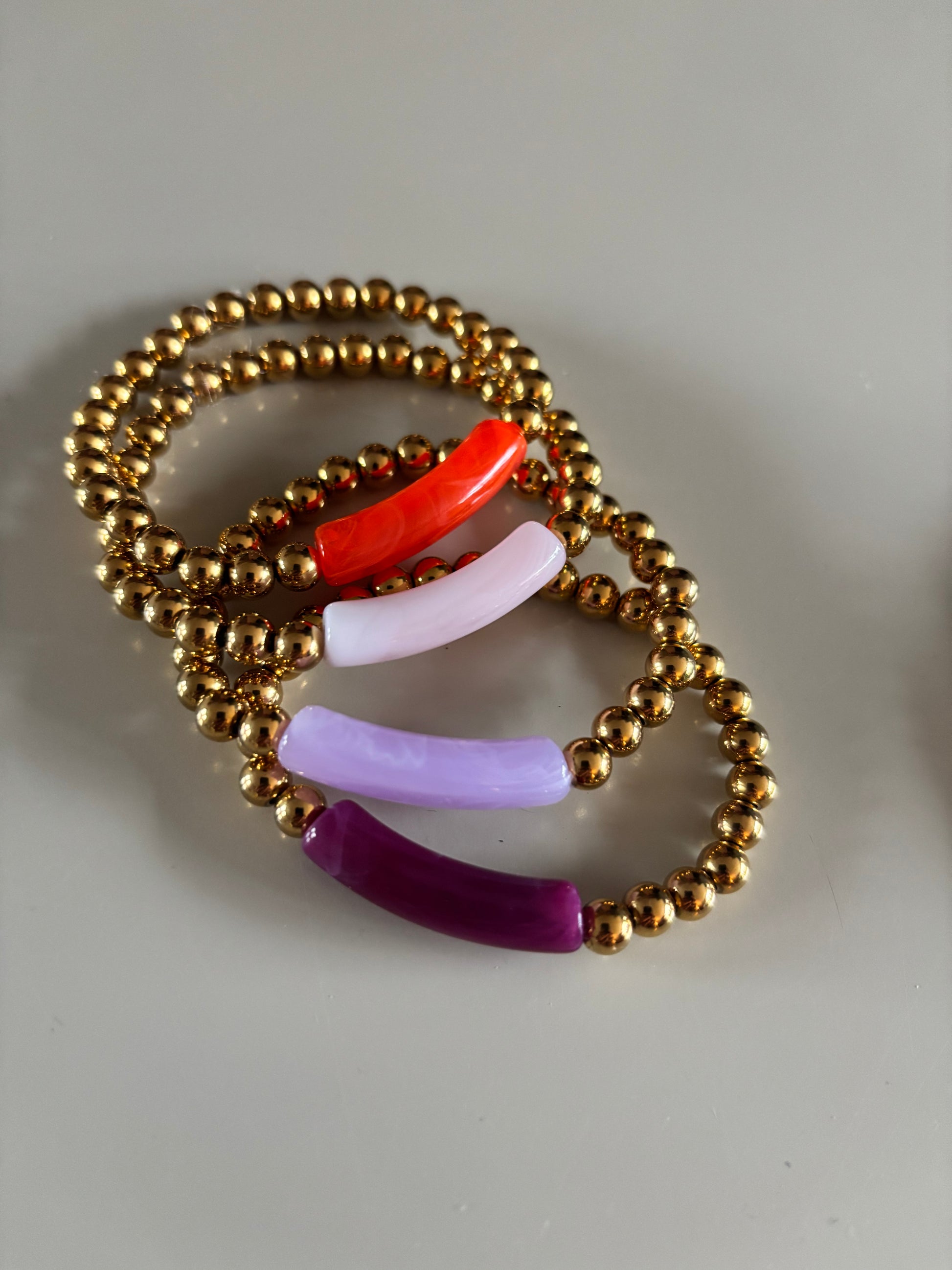 8k goldplated bolletjes en een grote, gebogen kunststof kraal met een subtiel gemarmerd effect in diverse kleuren zoals lila, fuchsia, oranje en mintgroen, paars, okergeel, koraal, zeegroen.
