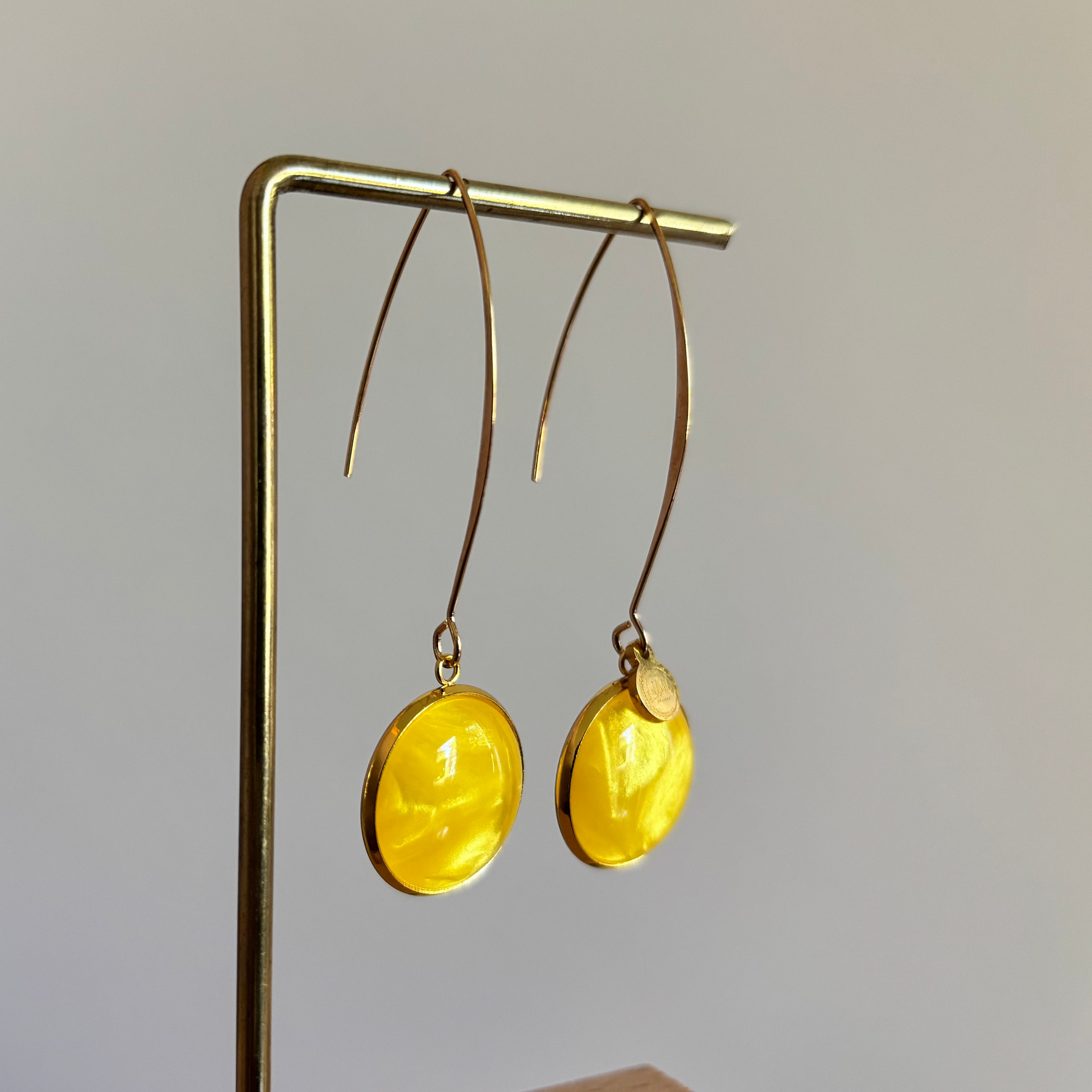 Lange goudkleurige oorbellen met een ronde, gele cabochon bedel van 18 mm