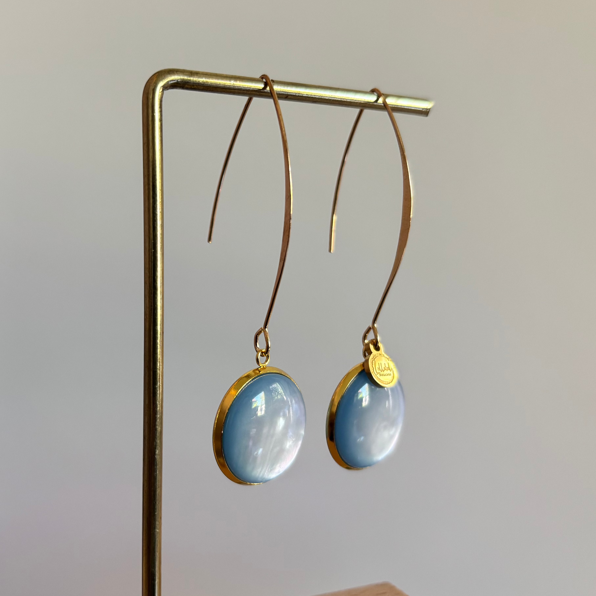 Lange goudkleurige oorbellen met een ronde, lichtblauwe cabochon bedel van 18 mm