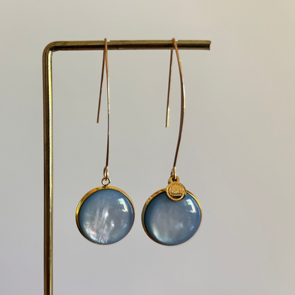 Lange goudkleurige oorbellen met een ronde, lichtblauwe cabochon bedel van 18 mm