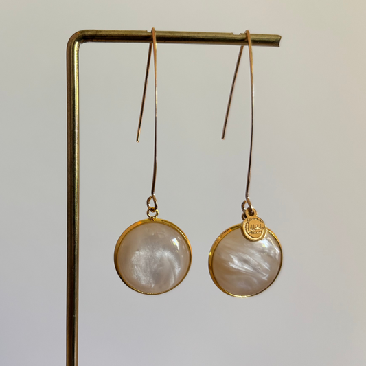 "Lange goudkleurige oorbellen met een ronde, parelmoer cabochon bedel van 18 mm hangend aan een display."