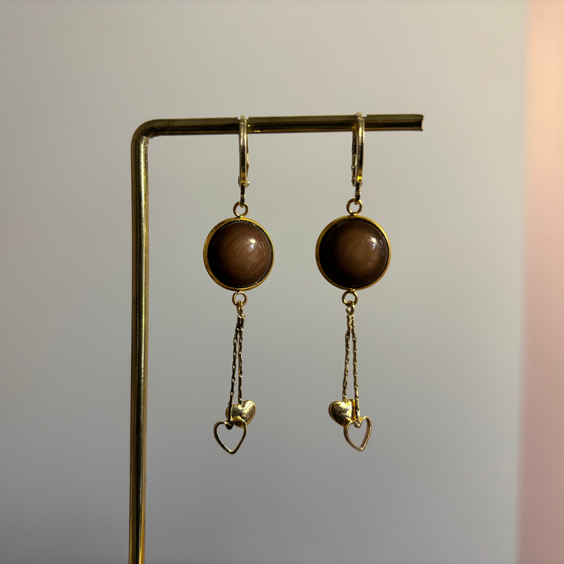 Korte oorbellen met donkerbruine cabochon en een hanger met twee hartjes, één open en één gesloten.