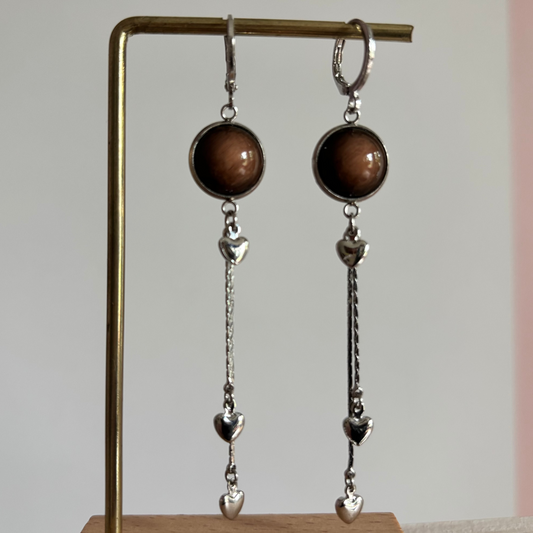 Zilverkleurige oorbellen met een ronde donkerbruine cabochonsteen en een hanger van een dichte zilveren hartjes.