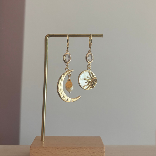 Asymmetrische oorbellen met een 14K gouden vergulde maan, glasbedel en een parelmoerhanger met daarin een 14K vergulde zon en zirkonia.