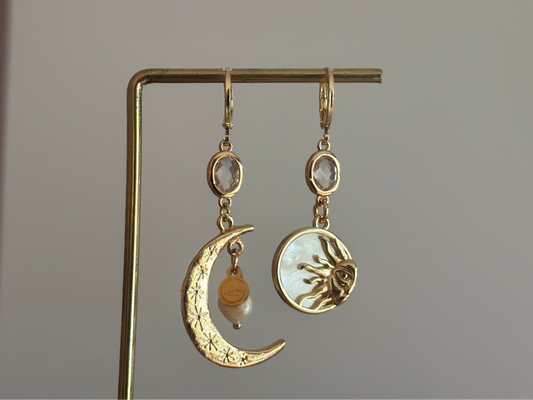 Asymmetrische oorbellen met een 14K gouden vergulde maan, glasbedel en een parelmoerhanger met daarin een 14K vergulde zon en zirkonia.