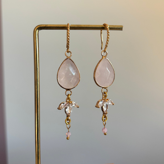 "Gouden oorbellen met een zachtroze steen, een trio van heldere kristallen en een klein roze kraaltje."