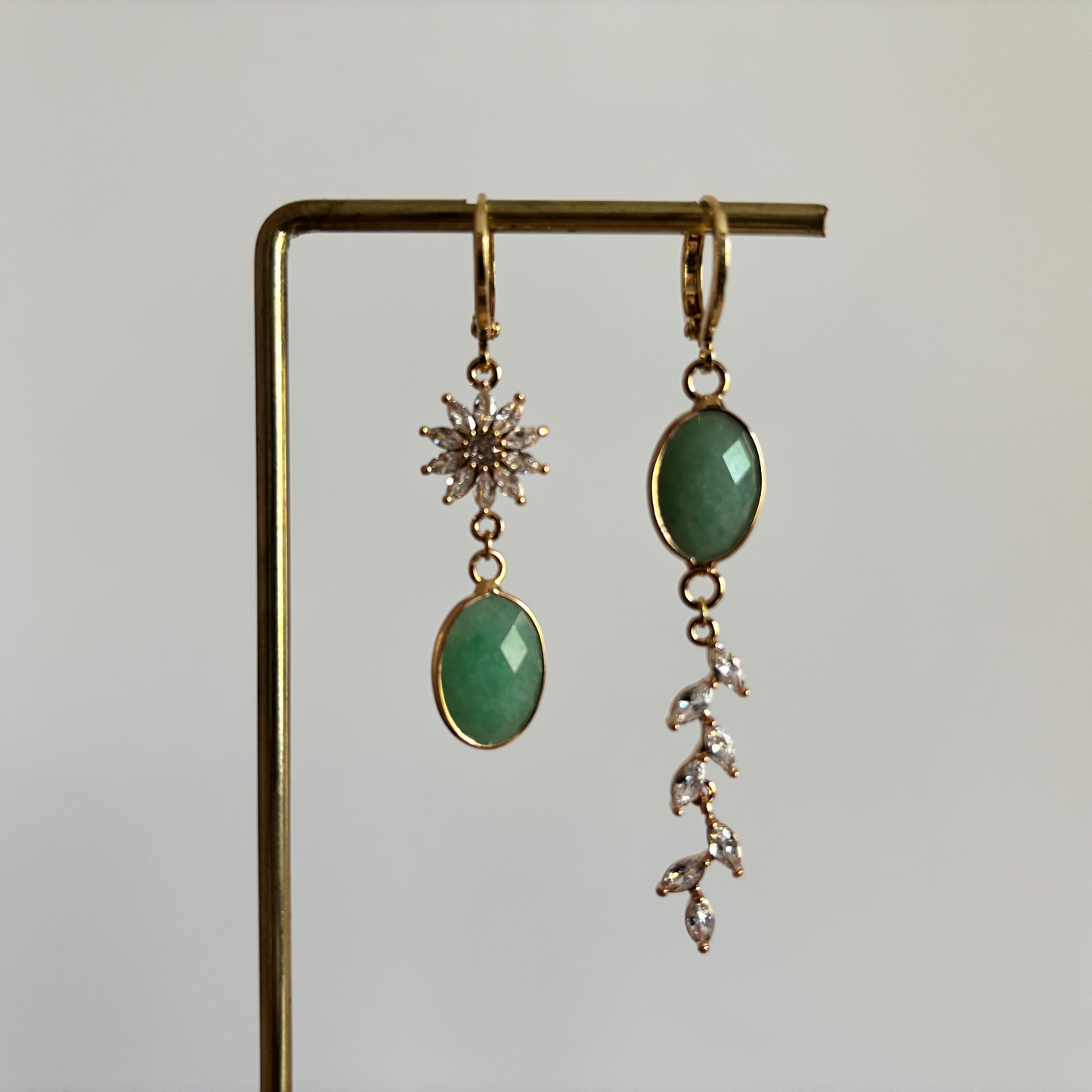 Asymmetrische set 14k vergulde oorringetjes Marietje met aan de ene kant een mintgroene natuursteen onder een zirkonia bloem en aan de andere kant een streng van zirkonia blaadjes.