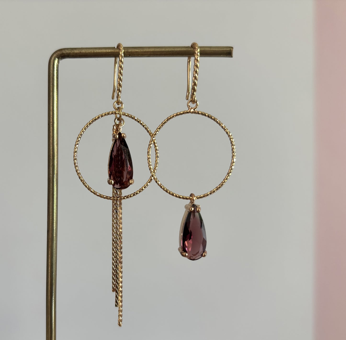 14k vergulde asymmetrische oorbellen Marly met bewerkte ronde ringen, bordeauxrode gefacetteerde druppelstenen en fijne kettinkjes.