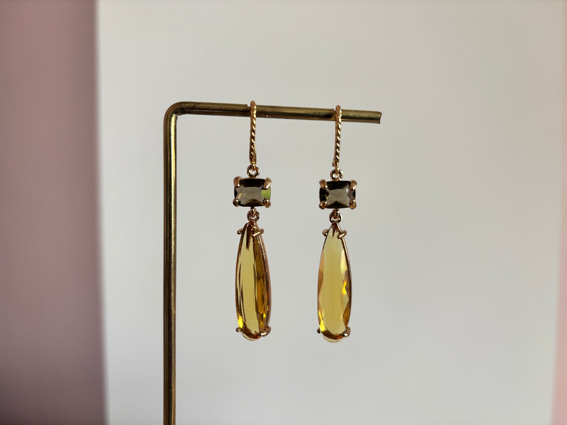 Gouden oorbellen Maya met een kleine rechthoekige rookgrijze steen en een lange honinggele kristallen druppel op een gouden standaard.