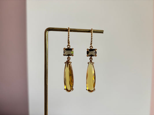 Gouden oorbellen Maya met een kleine rechthoekige rookgrijze steen en een lange honinggele kristallen druppel op een gouden standaard.