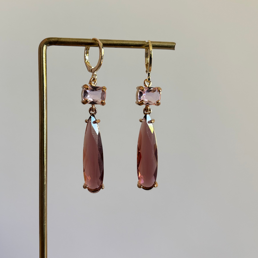 Goudkleurige oorbellen Maya met een kleine vierkante lichtroze steen en een lange burgundykleurige druppelvormige hanger van kristal.
