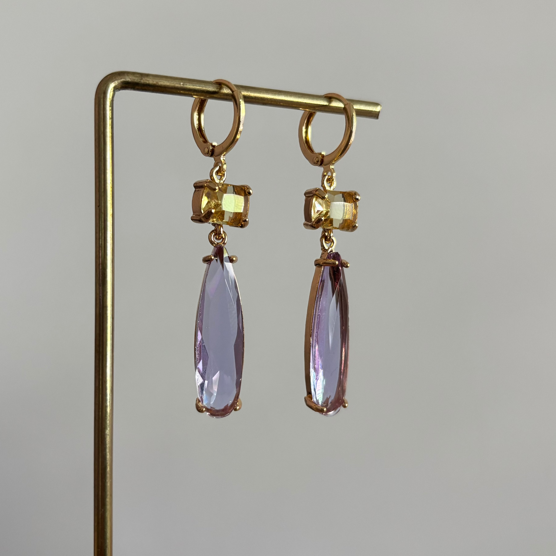 14k vergulde oorbellen model Maya met een vierkante gele kristallen steen en een hangende, lila druppelvormige kristalsteen.