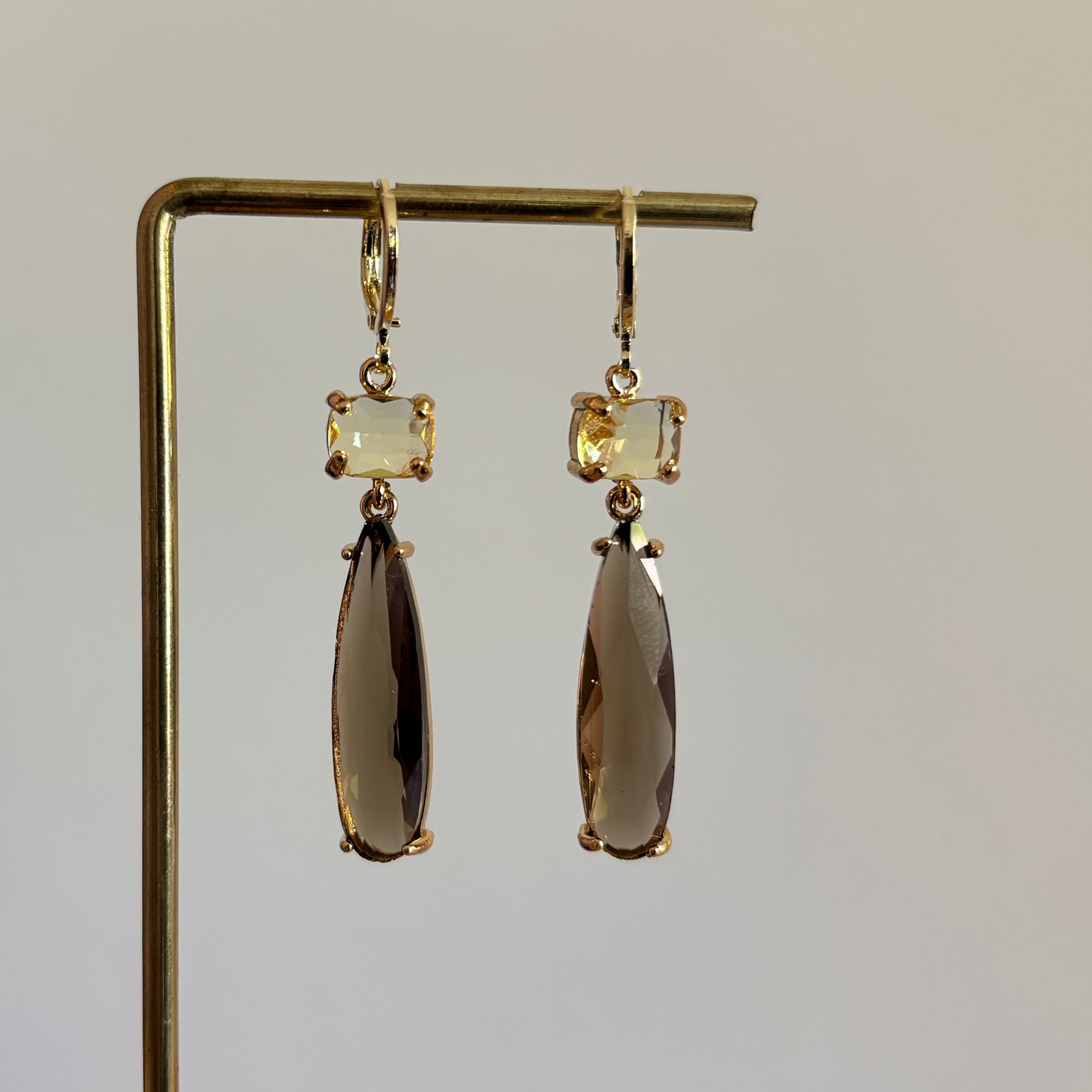 Goudkleurige oorbellen Maya met een kleine rechthoekige gele steen en een lange taupekleurige druppelvormige hanger van kristal